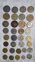 Photo showing 30 international coins of various sizes, colors, and designs arranged in rows on a white surface.