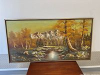 Full view of rectangular framed landscape painting showing autumn trees, reflective pond, and snow-capped mountains.