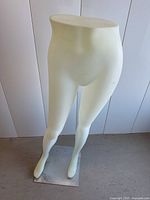 Front view of white male lower body mannequin from waist to feet showing smooth surface and metal base on concrete floor