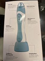 Photo showing the PMD Personal Microderm Elite Pro device on its charging base with labels highlighting features such as Luxe Caps, replaceable discs, slim ergonomic design, TruTear technology, and cordless rechargeable functionality.