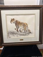 Full view of the framed artwork showing the lioness and cubs in grass, with a wide dark wooden frame and double matting.