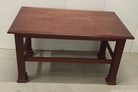 Front view of the small wooden coffee table showing rectangular top, lower shelf, and solid legs.