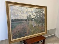 Framed impressionistic landscape image resembling Claude Monet with pathway and figures in a countryside setting resting on a small wooden table.