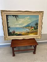 Full view of the oil painting in its carved wooden frame standing on a small wooden bench.