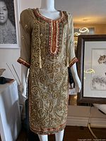 Full front view of beige women's dress with heavy gold bead embroidery and red accents, displayed on a mannequin.