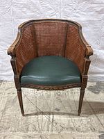 Front view of armchair showing carved frame, caned back and green leather seat