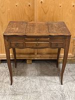 Front view closed with top flaps folded, showing three small drawers and tapered legs