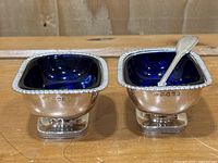 Front view of two salt cellars on pedestal feet; right cellar fitted with salt spoon