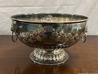 Front view of bowl showing floral garland and lion head ring handles on pedestal base