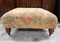 Front view of ottoman showing world map upholstery and turned wooden legs