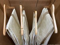 Four folded cream panels on wooden hangers inside a box