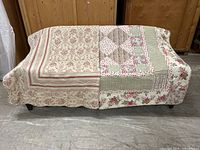 Two quilts draped side by side showing beige and red toile quilt (left) and floral & plaid patchwork quilt (right)