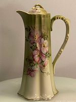 Front view of tall antique Nippon chocolate pot with hand painted pink flowers and gold accents on cream and green background.