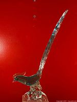 Side view of Murano glass pheasant showing textured green body, clear tail, and organic clear glass base against red background.