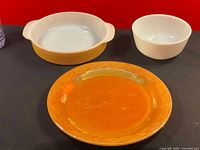 Three items displayed side by side: handled peach lustre round casserole dish, white milk glass bowl, peach lustre plate