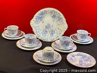 Front view of the full tea set showing cups on saucers, side plates in front, and cake plate in back on black and red background.