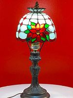 Full view of the Tiffany style stained glass bed lamp, showing the lamp base and lit floral stained glass shade against a red background.