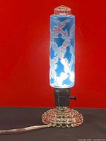 Front view of the vintage boudoir art glass lamp lit up showing the blue floral embossed glass globe and clear glass bubble base.