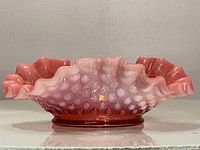 Side view showing ruffled edges, hobnail texture, and color gradient on the cranberry glass bonbon dish.