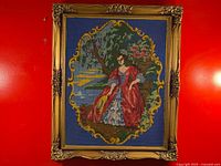 Full view of vintage needlepoint artwork of French aristocrat seated in garden, framed with carved wooden frame and glass cover on red background.