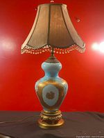 Full lamp with shade illuminating, showing blue and gold vase base and fabric shade fringe.