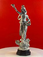 Front view of vintage silver coated figurine trophy on wooden hexagonal base against red background.