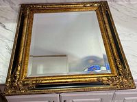 Full view of the vintage wooden framed mirror showing the detailed ornate gold and black carved frame and clear mirror surface.