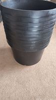 Side view of one large black plastic plant pot stacked to show ribbed sides and durable construction.