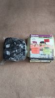 Inglesina Fast baby table chair in black fabric with attachment straps, still in plastic, next to its original box.