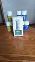 Front view of ONA Mist Dispenser box surrounded by 8 cans of ONA odor neutralizer mist in green and blue cans.
