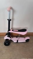 Side view of a pink children's scooter with a black seat and adjustable handlebar, showing the overall design and condition.