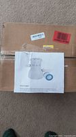 Photo of the pool filter pump inside a cardboard box with product information attached.