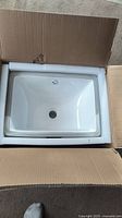 Overhead photo of new white porcelain sink inside original box packaging with foam padding.