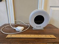 White AK1980 alarm clock with power adapter and cord, placed next to a ruler for size reference.