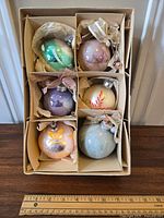 Six vintage glass ornaments in a divided cardboard box wrapped in tissue paper.