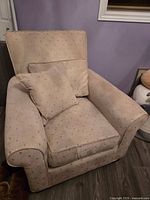 Full view of oversized beige armchair with matching cushions in fabric featuring gold sewn square patterns.