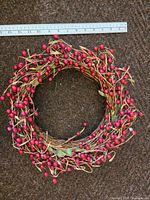 Top-down view of the cranberry wreath on a brown carpet background with a ruler showing about 14 inches diameter