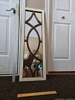 Front view showing full length of the narrow decorative mirror with white frame and brown geometric design within the mirror glass.