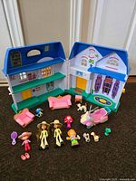 Photo of opened blue and white foldable plastic dollhouse with assorted dolls and accessories displayed in front.