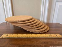 Eight round cork hot pads arranged in a slightly fanned out stack with a ruler showing approximate 7 inch diameter.