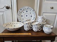 Full view of the Finlandia Royal Oak set arranged on a wooden table showing all items: serving plate, serving bowl, sugar bowl with lid and spoon, creamer, 8 teacups and 8 saucers.