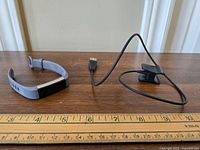Fitbit Alta HR tracker and charging cable on wooden surface, approximate length shown with ruler.