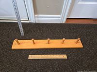 Horizontal view of the five peg wooden coat hooks with rulers showing length of about 18 inches.