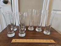 Six clear glass flute glasses arranged in front of a white door with a ruler indicating size.