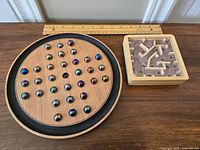 Photo showing the wooden circular Solitaire game board with marbles and the square wooden marble maze puzzle with pathways.