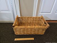 Front angle photo showing the woven basket with handles and a ruler for size reference.