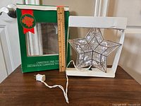 Photo showing light up star tree topper in front of its green original box with measurements shown by a ruler.