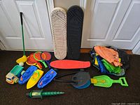 Photo showing assortment of outdoor and beach toys including skateboards, plastic boats, paddle ball sets, shovel, toy truck, golf club, ball, and green pump.