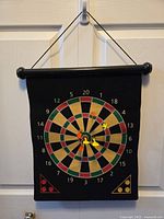 Dartboard hanging on door showing the traditional dart game side with numbered sections and 3 yellow magnetic darts sticking to the board.