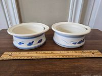 Front view of two pottery butter bowls with blue floral design, showing their size next to a ruler.
